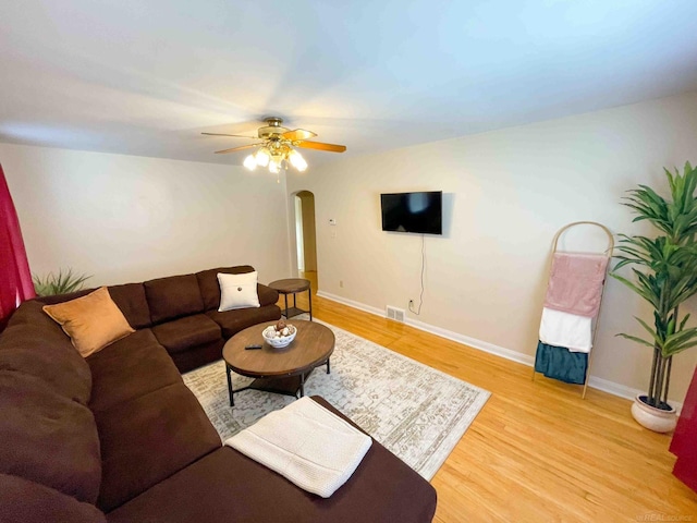 living room featuring visible vents, a ceiling fan, baseboards, arched walkways, and light wood-style flooring