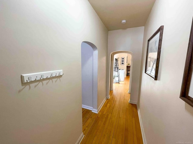 hall featuring arched walkways, baseboards, and light wood-style floors