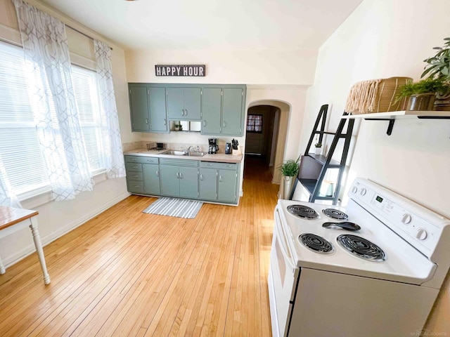kitchen featuring light wood-style floors, arched walkways, white range with electric stovetop, and light countertops