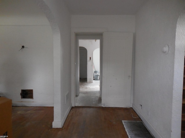 hall with baseboards, arched walkways, wood finished floors, and visible vents