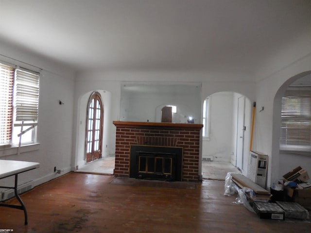 unfurnished living room with arched walkways, a fireplace, wood finished floors, and visible vents