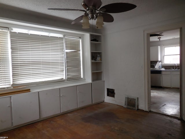 empty room with a sink, ceiling fan, wood finished floors, and visible vents