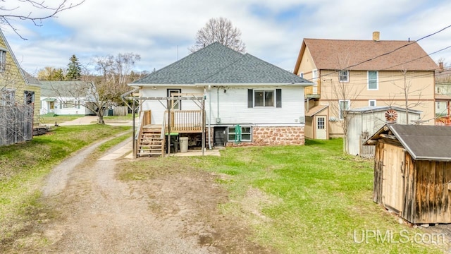 back of property featuring an outdoor structure, a shed, a shingled roof, a yard, and stairway