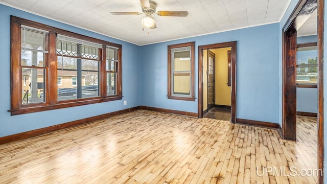 unfurnished room with wood-type flooring, a ceiling fan, baseboards, and crown molding