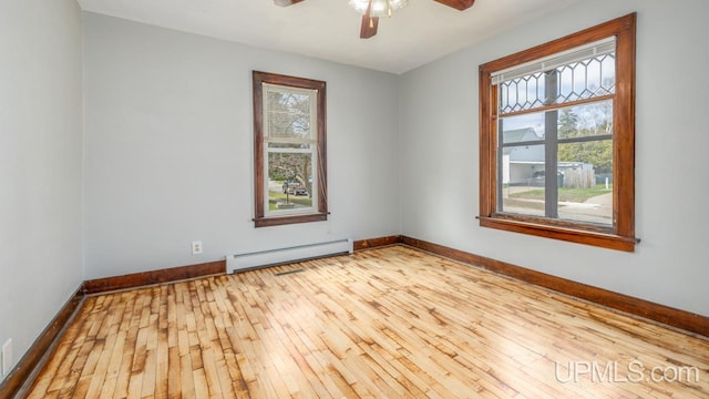 unfurnished room with a ceiling fan, baseboard heating, hardwood / wood-style flooring, and a healthy amount of sunlight