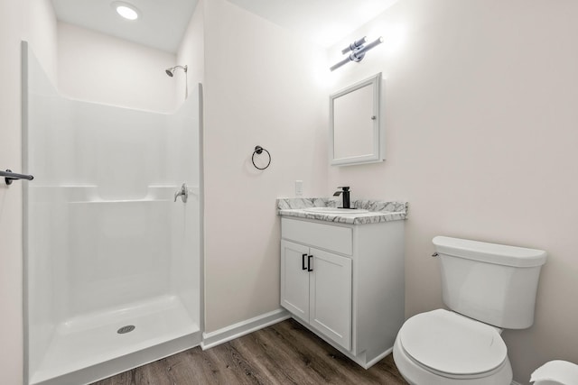 bathroom with vanity, wood finished floors, toilet, baseboards, and a stall shower