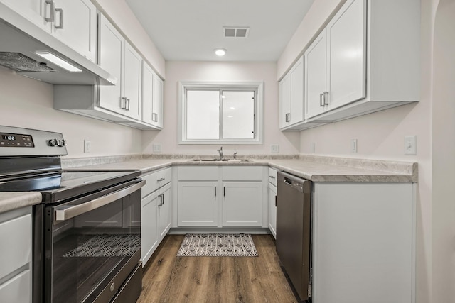 kitchen featuring dark wood-style floors, white cabinetry, under cabinet range hood, a sink, and appliances with stainless steel finishes