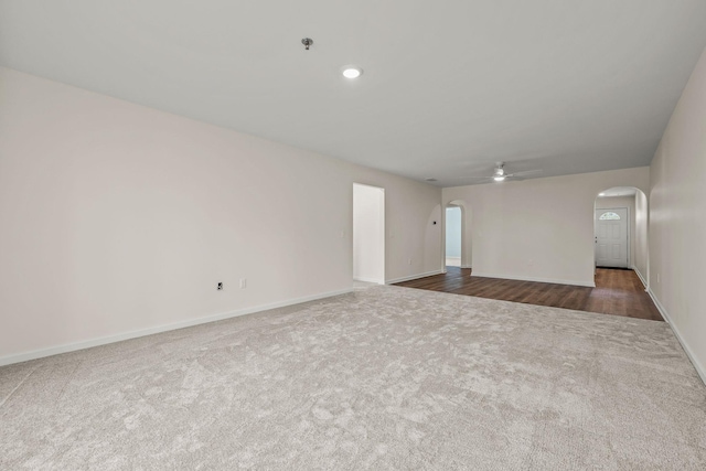 empty room featuring dark colored carpet, arched walkways, baseboards, and ceiling fan
