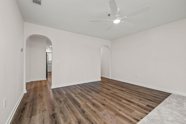empty room featuring visible vents, arched walkways, a ceiling fan, and wood finished floors