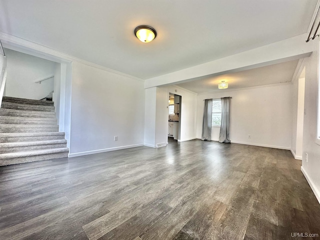 unfurnished living room featuring baseboards, dark wood finished floors, crown molding, and stairway