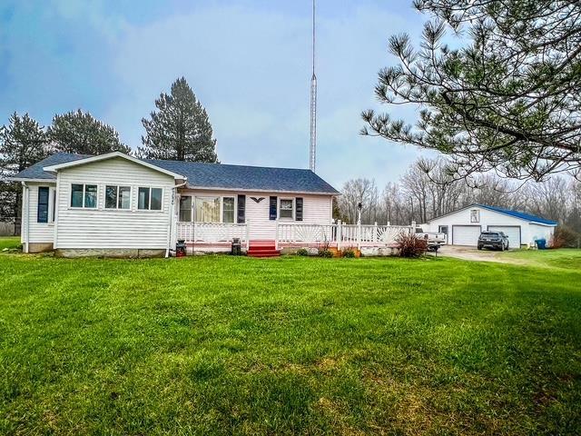 single story home with a detached garage, a wooden deck, an outbuilding, and a front lawn
