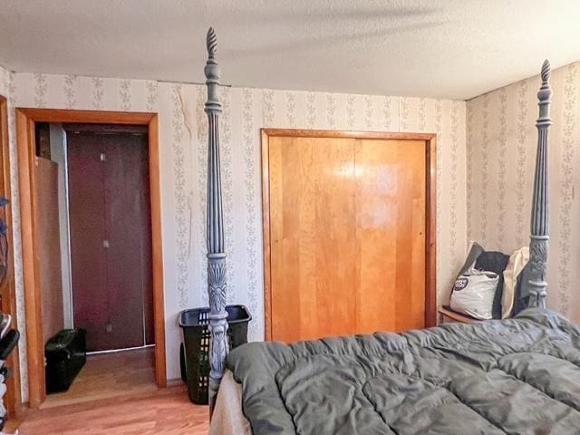 bedroom with light wood-type flooring, a textured ceiling, and wallpapered walls