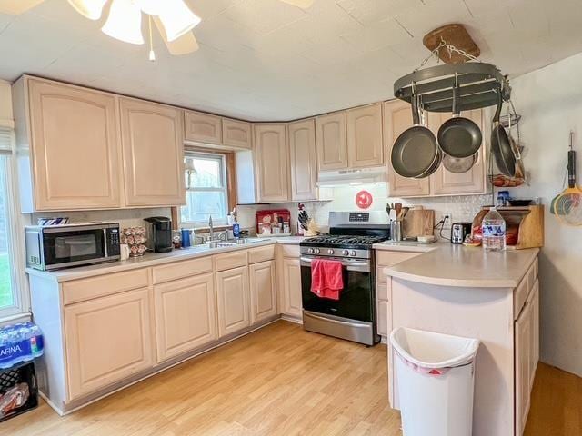 kitchen with appliances with stainless steel finishes, a sink, light countertops, light wood-style flooring, and under cabinet range hood