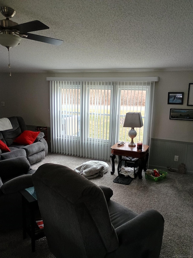 living area with carpet floors, a wainscoted wall, a ceiling fan, and a textured ceiling