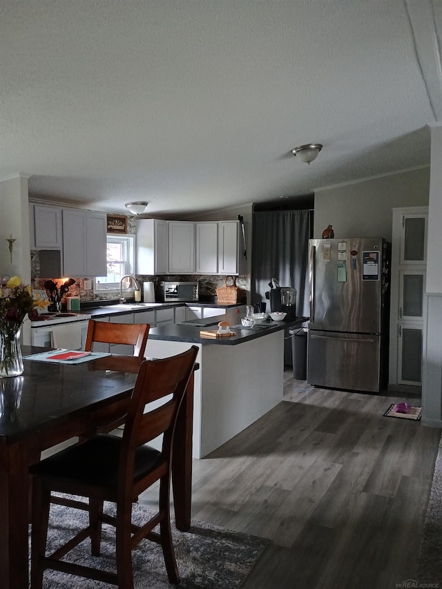 kitchen with decorative backsplash, wood finished floors, dark countertops, white cabinetry, and stainless steel appliances