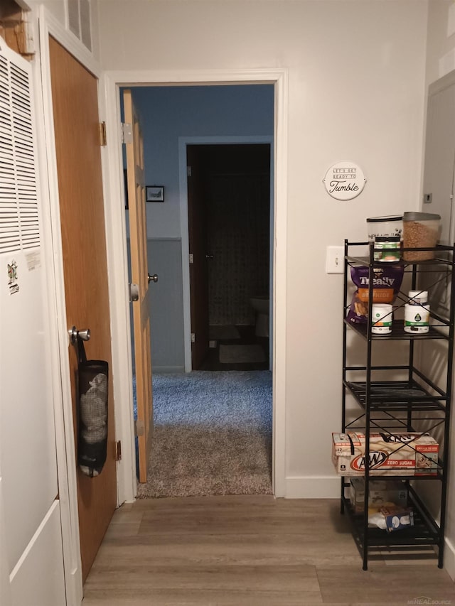 corridor with baseboards, a heating unit, wood finished floors, and visible vents
