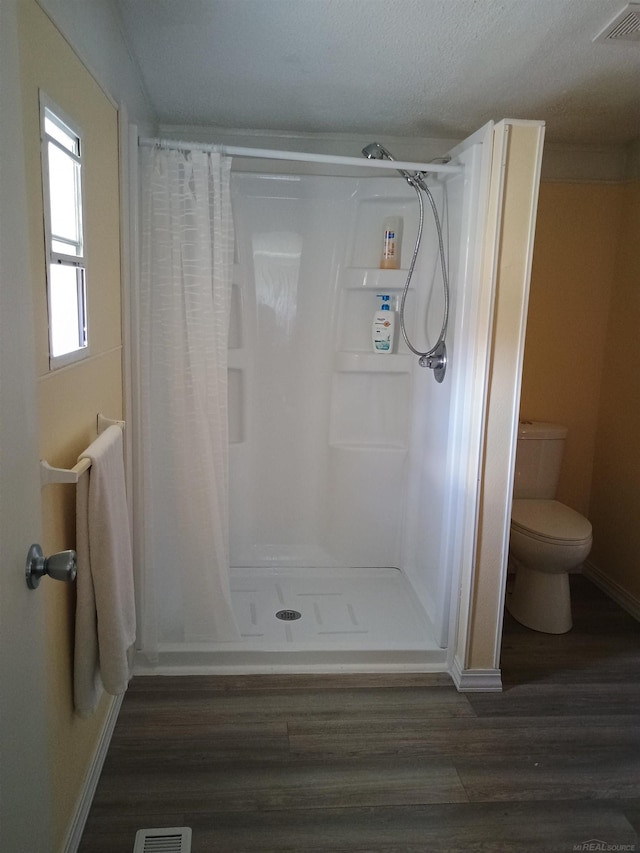 full bathroom featuring toilet, baseboards, wood finished floors, visible vents, and a stall shower