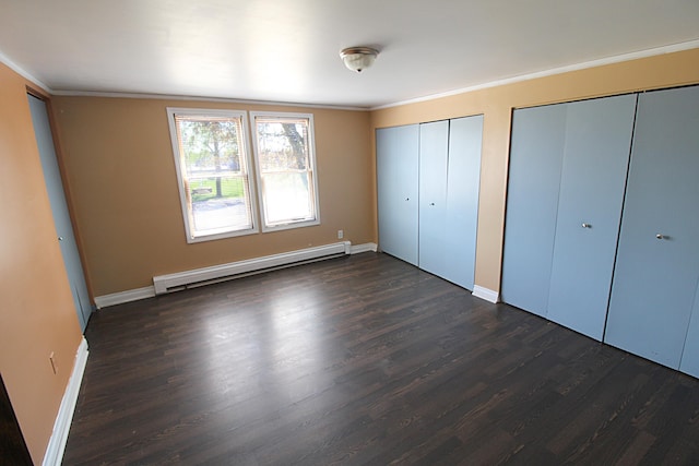 unfurnished bedroom featuring ornamental molding, dark wood finished floors, a baseboard heating unit, and two closets