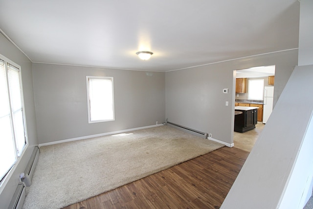 unfurnished living room with baseboards, light wood-style flooring, baseboard heating, and a wealth of natural light