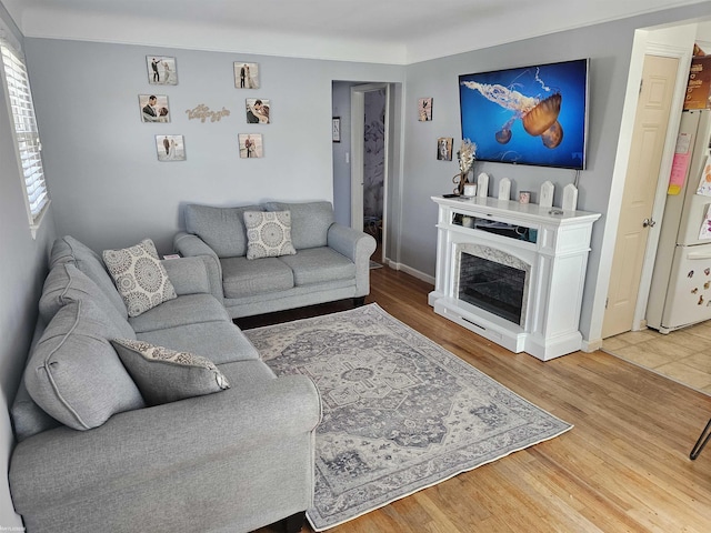 living room with a high end fireplace, baseboards, and light wood-type flooring