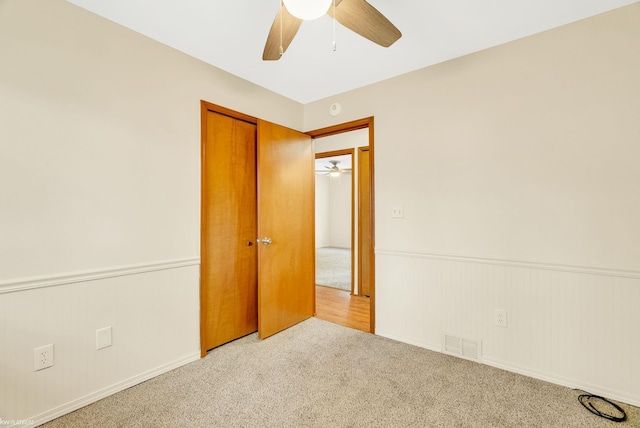 spare room featuring visible vents, carpet flooring, wainscoting, and ceiling fan