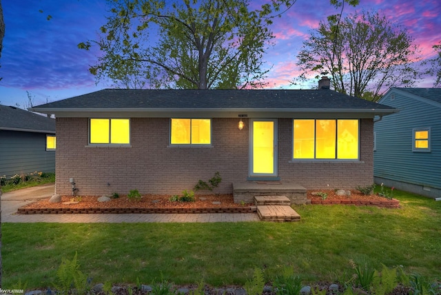 single story home with a yard, brick siding, a chimney, and a shingled roof