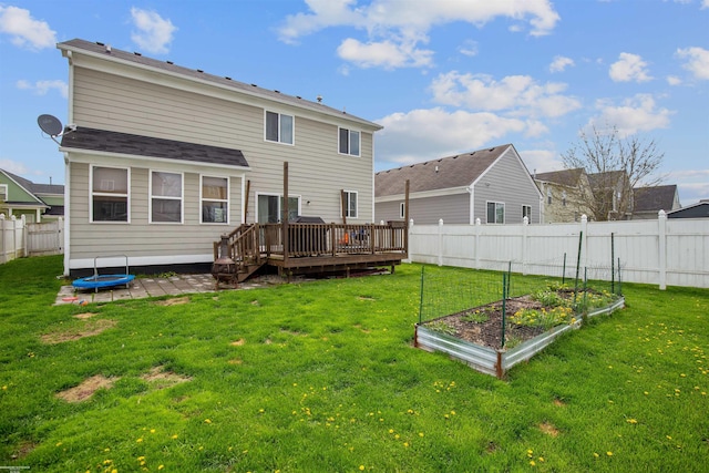 back of house with a wooden deck, a fenced backyard, a vegetable garden, a trampoline, and a yard
