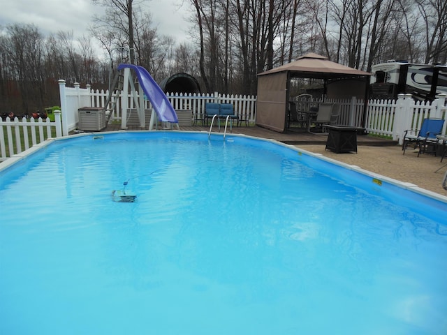 view of pool with a gazebo, a water slide, a fenced in pool, a fenced backyard, and central AC unit