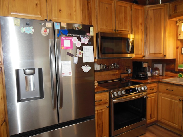 kitchen with a sink, dark countertops, brown cabinetry, and stainless steel appliances