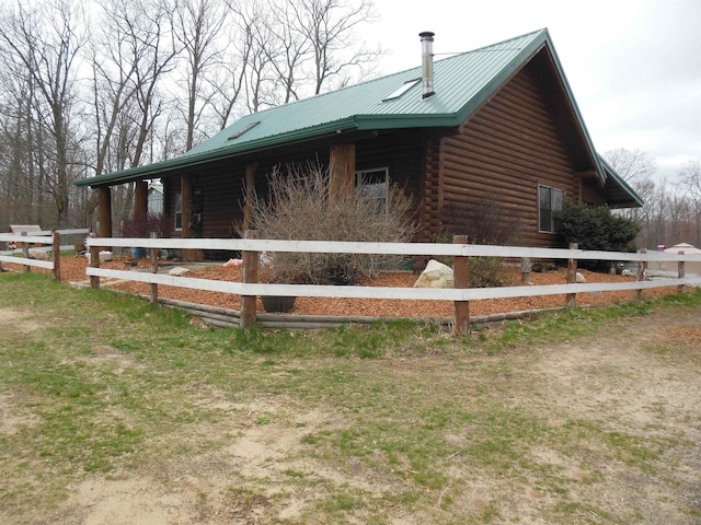 view of side of home with fence, log exterior, and metal roof