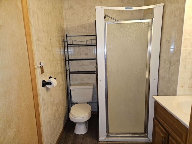 full bath with tile walls, a shower stall, wood finished floors, vanity, and toilet