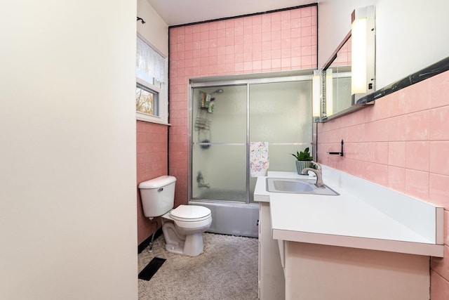 bathroom featuring toilet, tile walls, combined bath / shower with glass door, and vanity