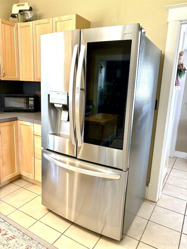 kitchen with stainless steel fridge, light brown cabinetry, light tile patterned floors, and black microwave