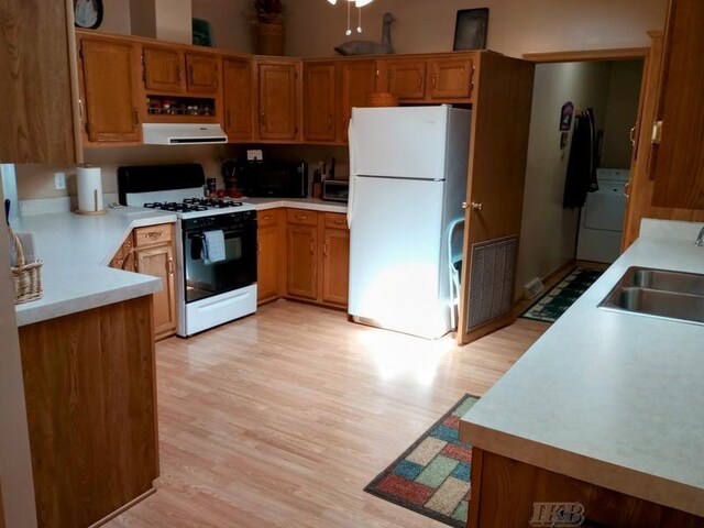 kitchen featuring exhaust hood, freestanding refrigerator, washer / dryer, visible vents, and range with gas cooktop