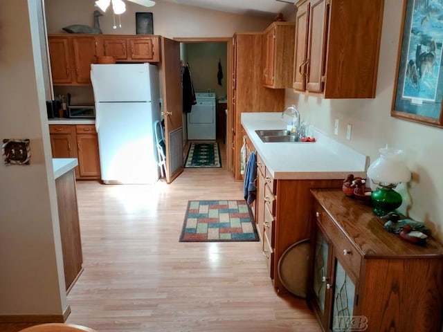 kitchen with freestanding refrigerator, light countertops, brown cabinets, a sink, and light wood-style flooring