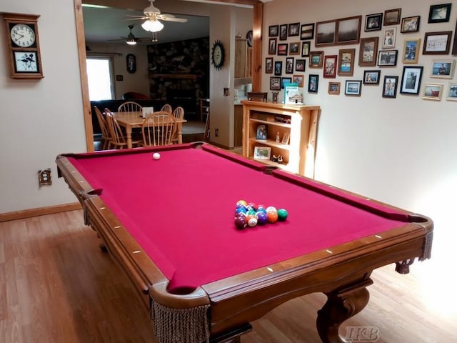 recreation room with pool table, a ceiling fan, a large fireplace, and wood finished floors