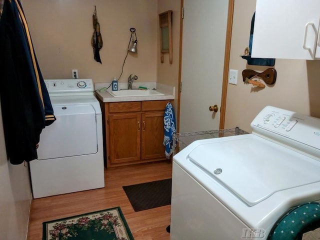 laundry area featuring light wood-type flooring, a sink, cabinet space, and washing machine and clothes dryer