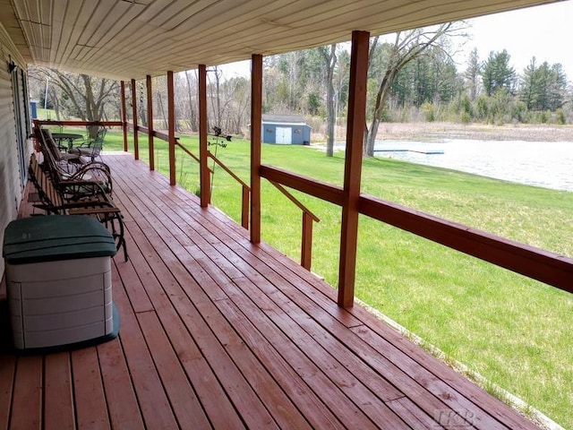 wooden terrace with an outdoor structure, a water view, a lawn, and a storage unit