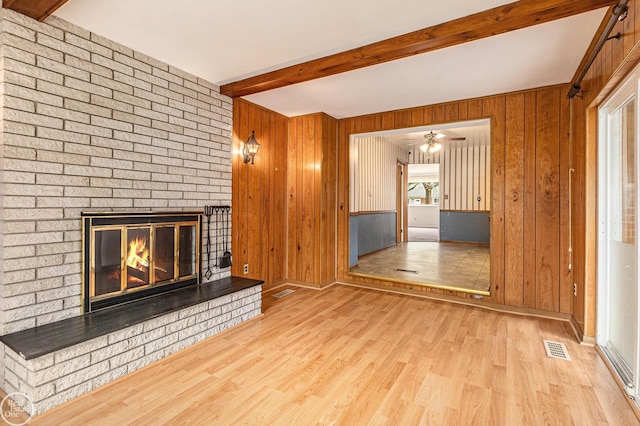 unfurnished living room featuring visible vents, a brick fireplace, wood walls, wood finished floors, and beamed ceiling