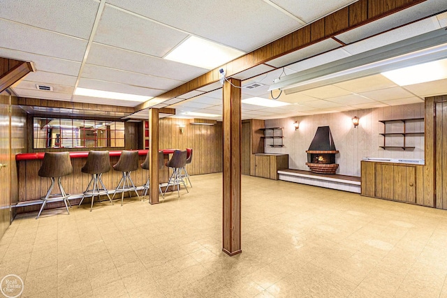 finished basement featuring a bar, wood walls, a drop ceiling, and tile patterned floors