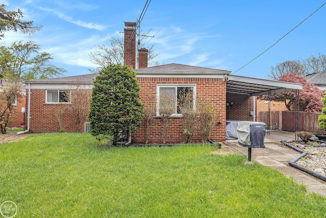 back of property with fence, an attached carport, a chimney, brick siding, and a lawn