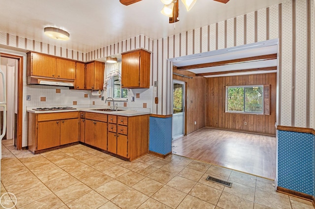 kitchen with gas cooktop, a sink, light countertops, under cabinet range hood, and wallpapered walls