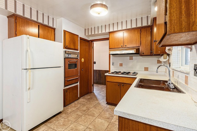 kitchen featuring freestanding refrigerator, brown cabinets, wall oven, and a sink