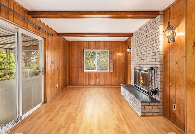 unfurnished living room with wood walls, beamed ceiling, a brick fireplace, and light wood finished floors