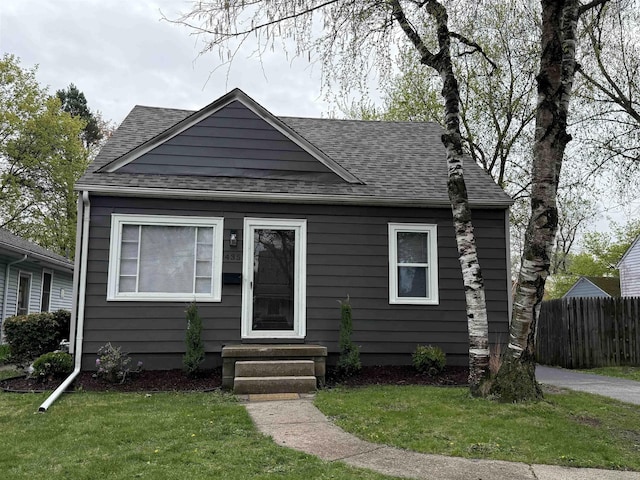 bungalow with fence, a shingled roof, and a front yard