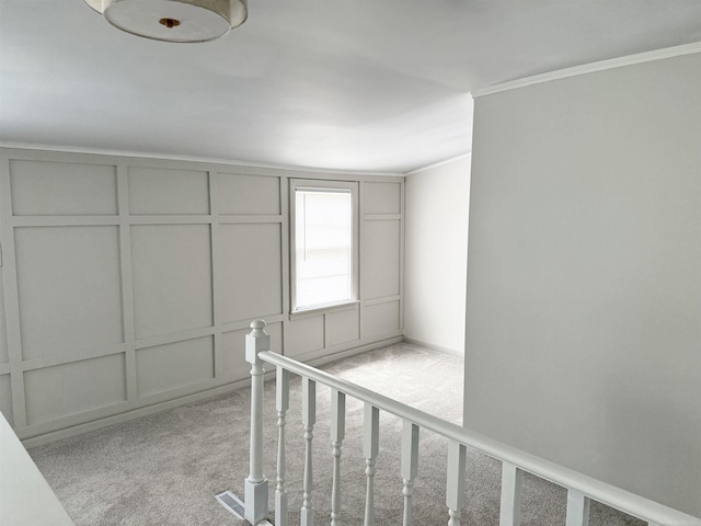 stairs featuring ornamental molding, a decorative wall, and carpet flooring