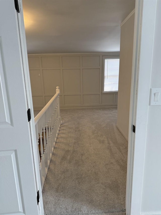hall with an upstairs landing, a decorative wall, and light carpet