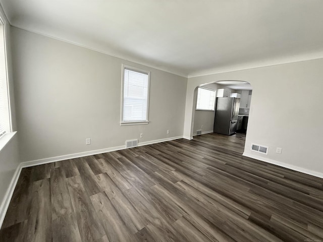 spare room featuring arched walkways, visible vents, and dark wood-type flooring