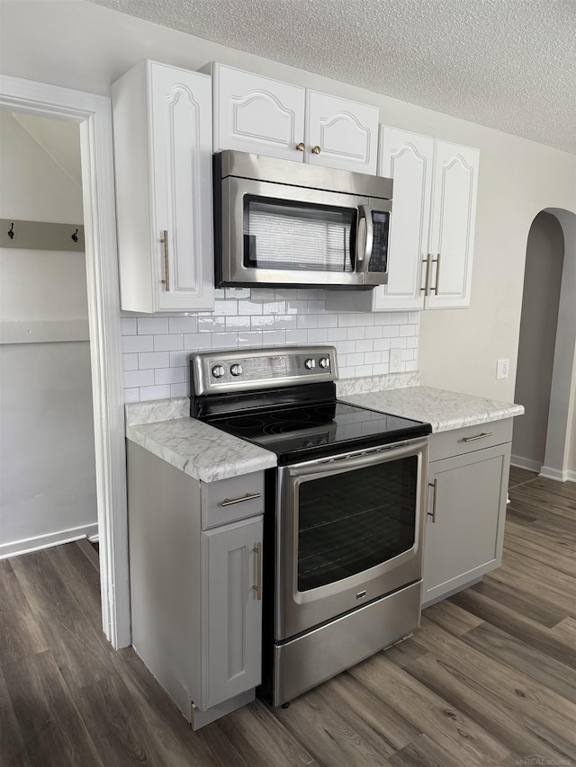 kitchen with decorative backsplash, a textured ceiling, appliances with stainless steel finishes, arched walkways, and dark wood-style floors