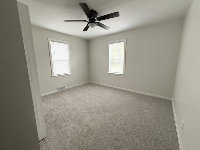 carpeted empty room featuring a ceiling fan, baseboards, visible vents, and plenty of natural light